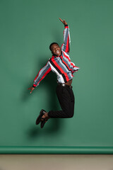 Studio shot of african man in bright shirt jumping isolated over dark green color background. Wow...