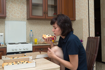 A hungry woman enjoys eating a large slice of pizza while sitting kitchen.