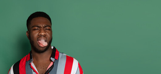 Funny young african man making faces isolated on green studio background with copyspace for ad.