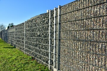 Moderner Sichtschutzzaun aus mit Naturstein gefüllten Gabionen um ein Neubaugebiet