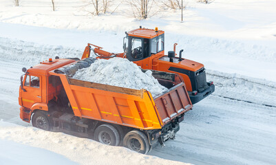 Big orange tractor cleans up snow from the road and loads it into the truck. Cleaning and cleaning...