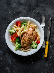 Casarecce pasta with broccoli, cherry tomatoes and baked chicken breast on a dark background, top view