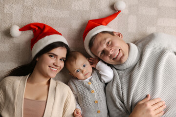 Fototapeta premium Happy couple with cute baby on floor, top view. Christmas celebration