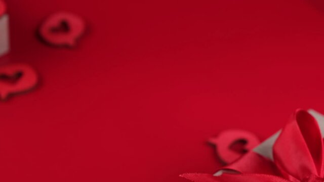 composition with a gift box tied with a red ribbon with a bow, hearts close-up on a red background. Concept for lovers or Valentine's Day