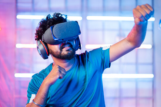 Young man with VR or virtual reality goggles or headphones dancing on neon light staged backgound - concept of modern technological experience.