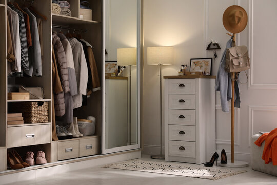 Wardrobe closet with different stylish clothes, shoes and home stuff in room
