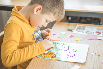 Little boy being creative making homemade do it yourself  dinosaur mosaic. Supporting creativity, learning by doing, learning through experience. Helping child gain access to a creative way of seeing.