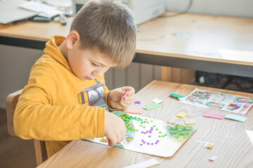 Little boy being creative making homemade do it yourself  dinosaur mosaic. Supporting creativity, learning by doing, learning through experience. Helping child gain access to a creative way of seeing.