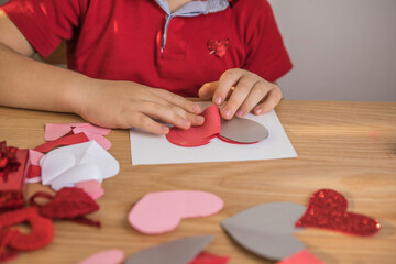 DIY holiday card with red paper heart, symbol of love. Kid boy makes Mother's Day, Valentine's Day, greeting card. Hobby, children art concept, gift with your own hands, DIY Ideas for children. Happy 