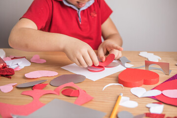 DIY holiday card with red paper heart, symbol of love. Kid boy makes Mother's Day, Valentine's Day, greeting card. Hobby, children art concept, gift with your own hands, DIY Ideas for children