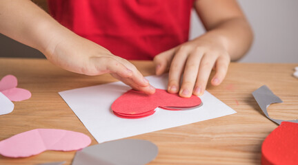 DIY holiday card with red paper heart, symbol of love. Kid boy makes Mother's Day, Valentine's Day,...