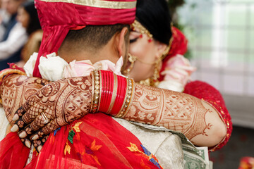 Back view of an Indian man in red turban hugging bride in a traditional red dress A closeup shot of...