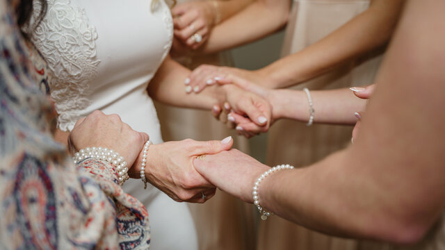 Cropped photo of Bridesmaids holding hands of the bride Support and love concept Morning preparations of the bride close up Bride in white lace dress 