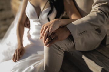 Closeup of the young brunette bride and groom sitting together on their wedding day the bride in beautiful gown and groom in beige suit married happy and romantic Cropped view