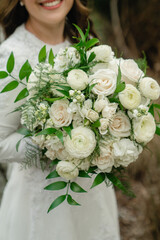 Beautiful wedding bouquet of  white roses in hands of the Bride in white lace gown holding an elegant bouquet made of white flowers and greenery Cropped photo