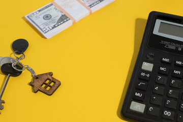 Buying a home. Keys with a keychain in the form of a house, money and a calculator on a yellow background with a place for the text. real estate for sale