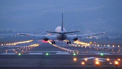 Passenger aircraft landing at night, telephoto view from end of runway with straight perspective. Bright approach and edge lights, flashlights at tail and wings of airliner