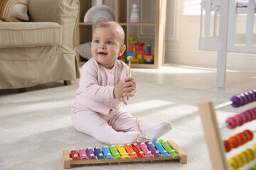 Cute baby girl playing with xylophone on floor at home