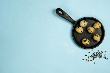 A flat shot of fried eggs in a cast iron pan on a blue background.
Quail eggs in a frying pan. Place for your text.