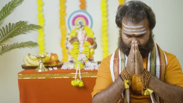Rack focus shot, holy saint or god man praying by chanting matras in front of ganesh idol during ganesh Festival - concept of religious or cultural offering and spiritual beliefs