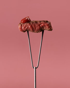 Delicious roasted meat on fork against pink background