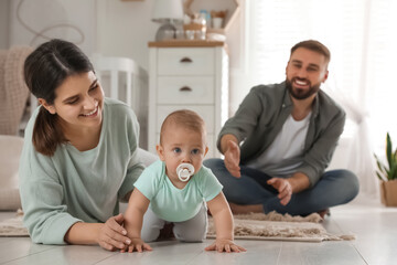 Happy parents helping their baby to crawl on floor at home