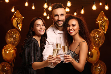 Happy friends with glasses of sparkling wine celebrating New Year indoors