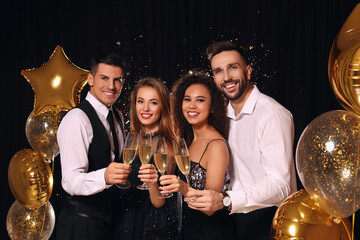 Happy friends with glasses of sparkling wine celebrating New Year on black background