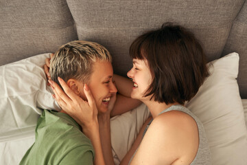 Young laughing lesbian couple rest and hug on bed