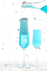 Two glasses with blue champagne and a bottle on a white background. Flying confetti. New Year or Christmas concept.