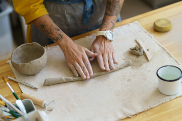 Artist working with raw clay. Hands of female craft ceramics maker molding wet pot on table in workshop studio. Art classes student or master making pottery handmade. Small business and craftsmanship