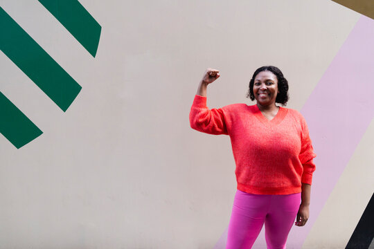 Smiling plus size woman flexing muscle in front of wall