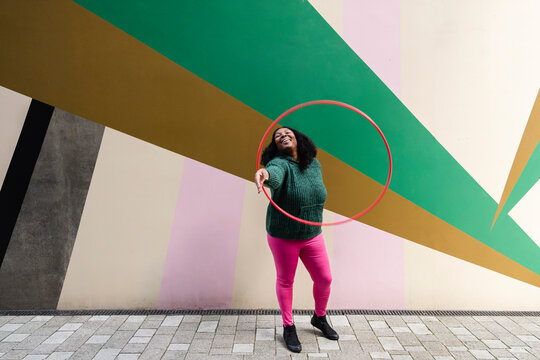 Cheerful plus size woman playing with plastic hoop on footpath