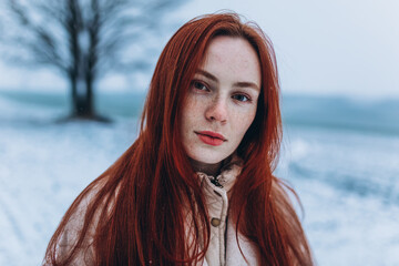 Close up red haired freckled woman portrait outdoor in winter snowy park