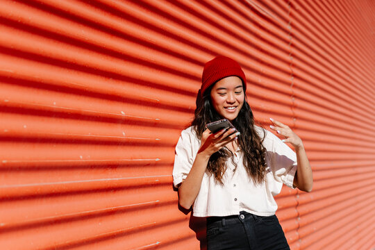 Woman sending voicemail through mobile phone at red wall