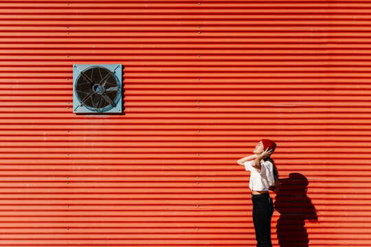 Woman wearing knit hat by red corrugated wall on sunny day