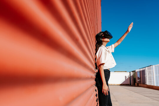 Young woman with virtual reality headset leaning on red wall