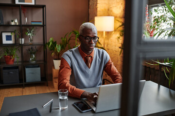 African young businessman concentrating on his online work typing on laptop while sitting at his workplace at office