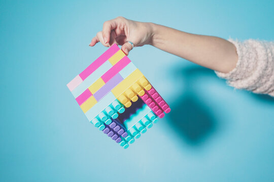 Arm of woman holding colorful cube made of pastel colored toy blocks