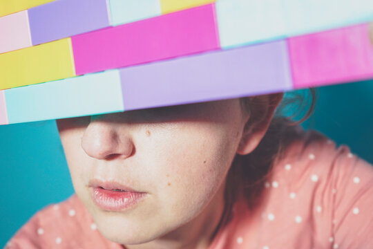 Face of adult woman hiding eyes behind toy blocks