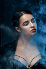 young brunette woman with professional makeup in a black jacket in the studio. multicolored light with smoke