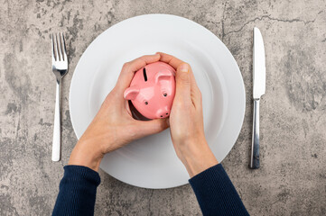 Eine Frau hält ein Sparschwein in den Händen auf einem Teller. Konzept Kosten für Lebensmittel