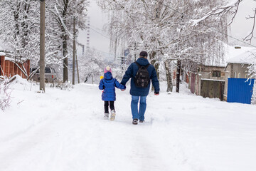 Fototapeta na wymiar Dad and daughter go for a walk on a snowy road on a winter day. Winter fun