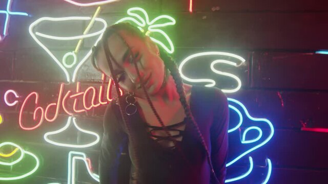 Hot amazon woman with pigtails dancing, posing with neon light at background. Close-up of brunette girl dancing in smoke 4K, UHD