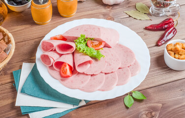 Sliced ham on a white plate on a wooden background.
