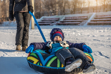 A happy child with his mother is tubing with a park from a slide. A fun winter weekend in the park...