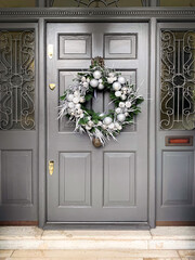 Christmas wreath: festive elegant charming christmasy themed winter natural wreath on a grey wooden door. Wreath decorated with silver sticks, baubles and pine cones
