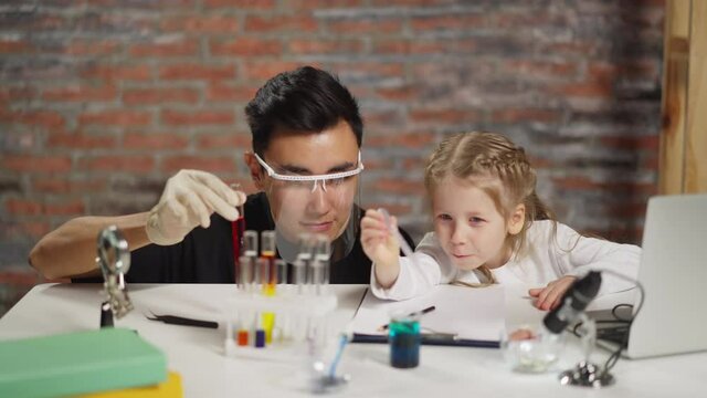 Asian teacher supports girl dropping reagent into beaker