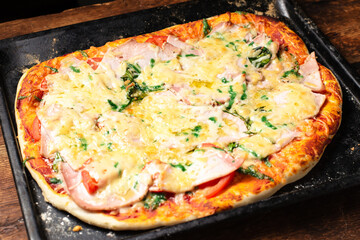 Homemade pizza on a baking sheet. Pizza with sausage, tomatoes, cheese.
