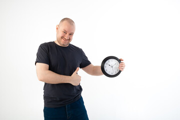 Deadline concept, time management. A satisfied man in a T-shirt holds a large clock. Isolated on a white background.